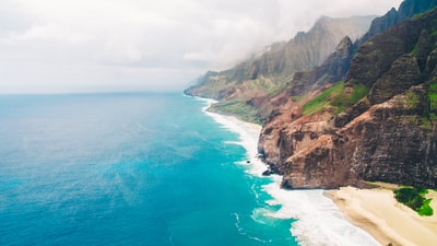 白天蓝海边的棕绿色山峦